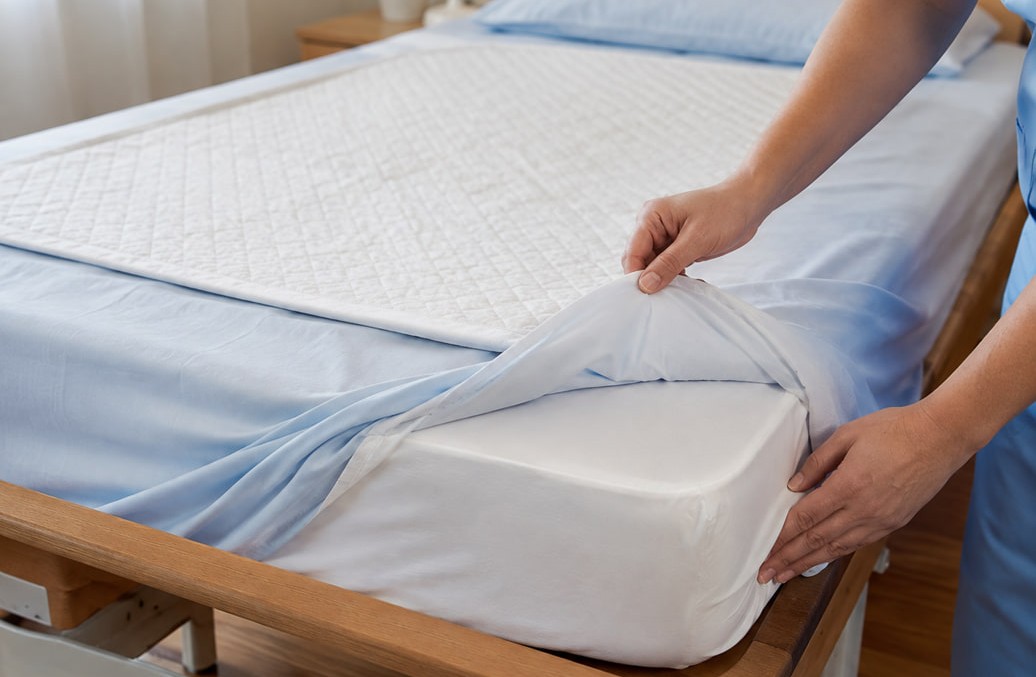 Traverse e coprimaterasso in un letto mostrate da una OSS fuori dall'inquadratura | HIP Sistema Letto